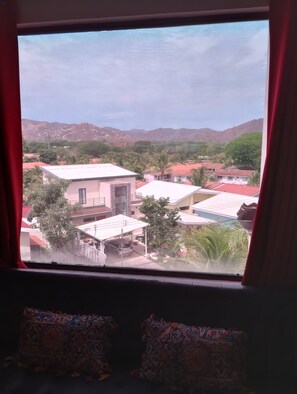 Blick durch ein Fenster auf eine Wohngegend mit Häusern, einem Auto und einem Berg im Hintergrund.