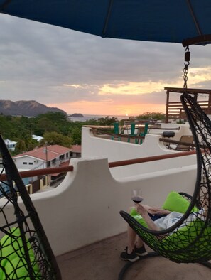 Ein Balkon mit einer Hängematte, Blick auf den Sonnenuntergang und ein Berg in der Ferne.