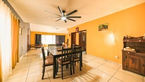 Un comedor con ventilador de techo, una mesa de comedor con sillas y una zona de cocina con armarios.