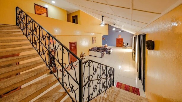 Una escalera con barandillas de metal decoradas, un techo alto y un interior luminoso.
