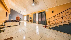 Un salón amplio con sofá, televisor y escalera con barandillas decorativas.