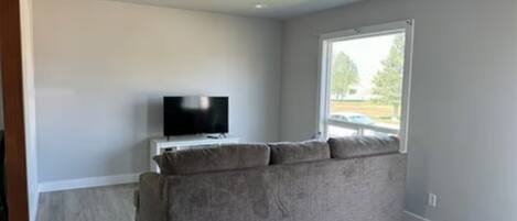 A room with a grey sofa, a television, and a window.