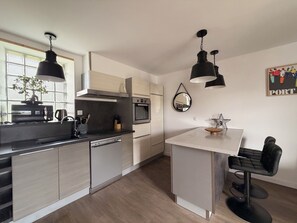 A modern kitchen with a central island, built-in oven, and pendant lighting. - Nice little house 5mn walk from the beach (Ploemeur)