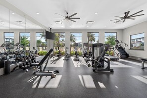 Ein modernes Fitnessstudio mit verschiedenen Trainingsgeräten, großen Fenstern und Deckenventilatoren.