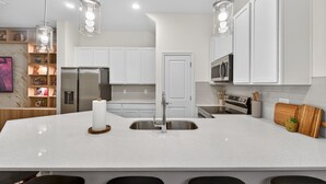 Una cucina moderna con mobili bianchi, elettrodomestici in acciaio inossidabile e luci a sospensione.