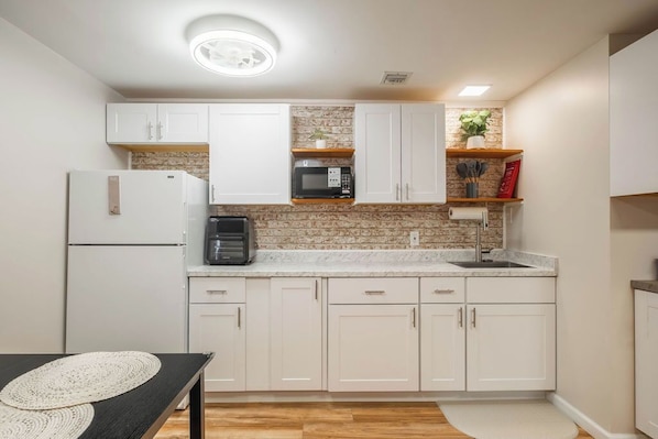 A modern kitchen with white cabinets, a granite countertop, a built-in microwave, and a coffee maker.