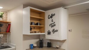 A kitchen with a coffee and tea bar sign, a coffee maker, and a kettle on the counter.