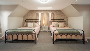 A bedroom with two beds, a brick wall, a window with curtains, and a ceiling light.