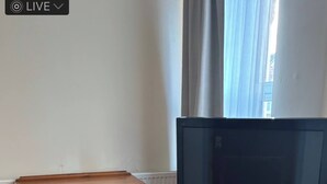 A wooden dresser, a television on a wooden stand, and a patterned rug on a wooden floor.