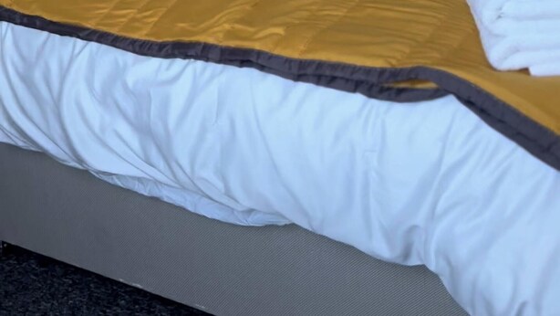A neatly made bed with a white and yellow bedspread, a wooden nightstand with a lamp, and a gray headboard.