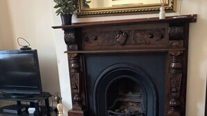 A room with a fireplace, a bed with a yellow bedspread, a television on a stand, and a framed picture above the fireplace.