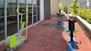 Un área de fitness al aire libre con equipo de ejercicio, un muro de cristal y vistas a la ciudad.