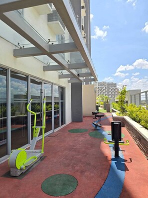 Ein Outdoor-Fitnessbereich mit Trainingsgeräten, einer Glaswand und Blick auf eine Stadtansicht.