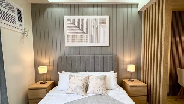 Un dormitorio moderno con una cama grande, dos mesitas de noche con lámparas, un cabecero y una obra de arte colgada en la pared.
