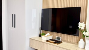 Una habitación moderna con un televisor montado en una pared de madera, un armario blanco y un escritorio de madera con una planta y un reloj.
