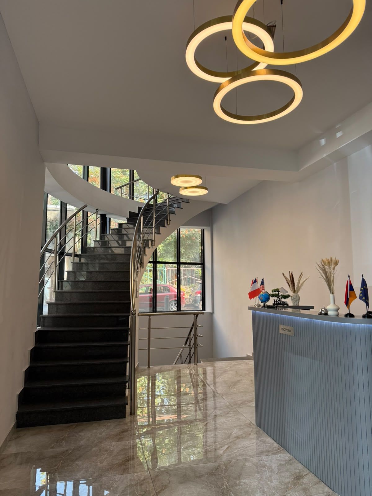 A modern reception area with a marble floor, a reception desk, and a staircase with metal railings.