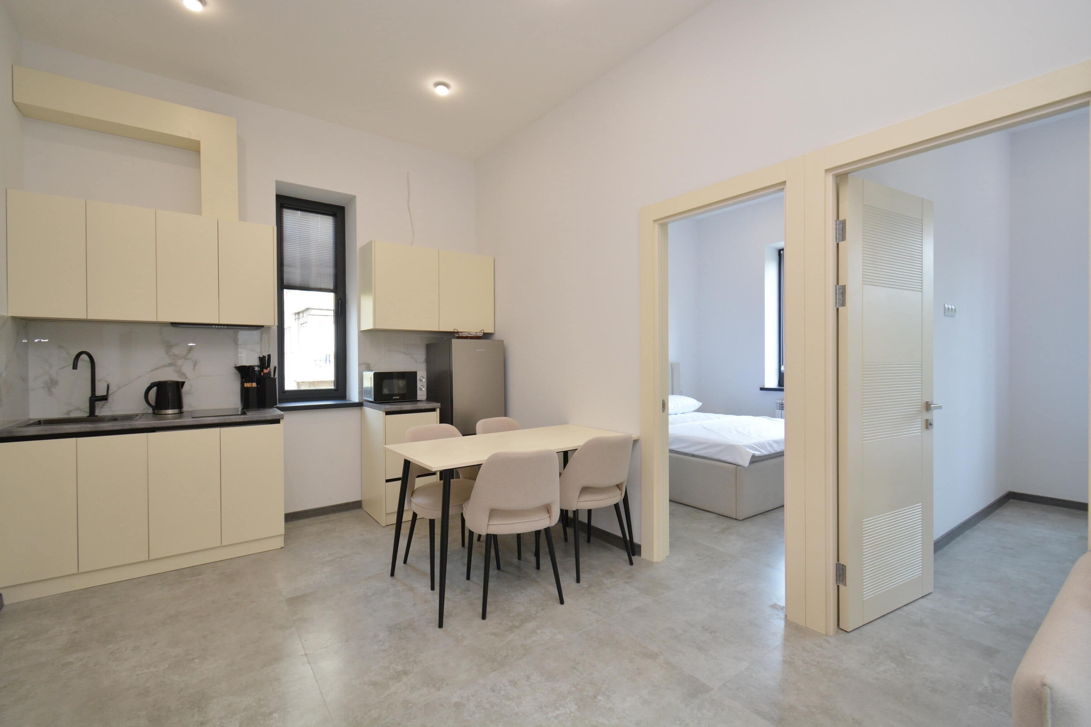 A modern kitchen with a dining area, a bed, and a door leading to another room.