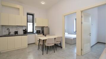 A modern kitchen with a dining area, a bed, and a door leading to another room.