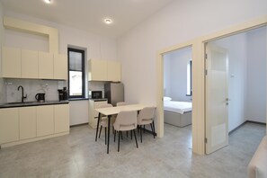 A modern kitchen with a dining area, a bed, and a door leading to another room.