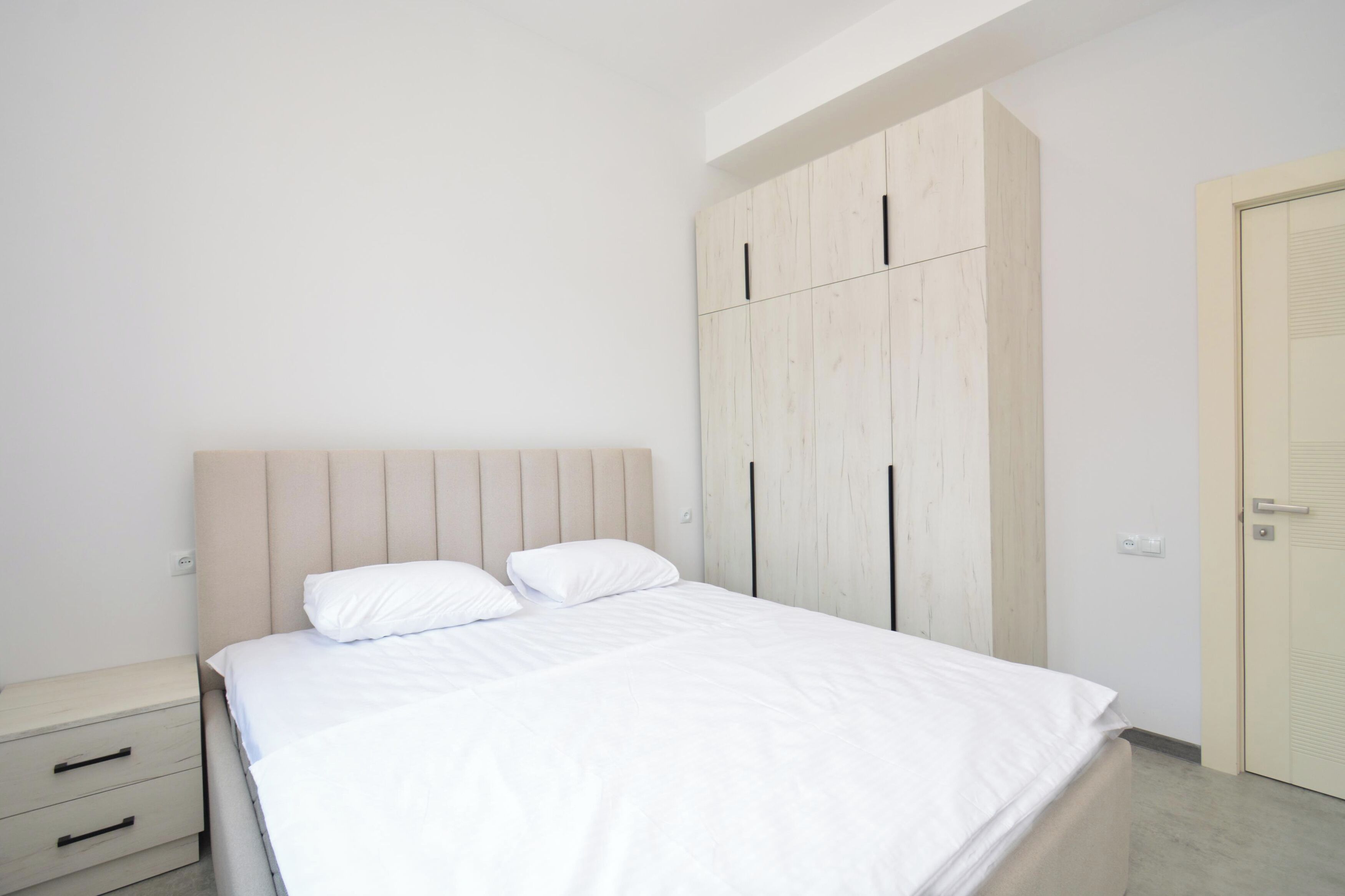 A bedroom with a bed, a nightstand, a wardrobe, and a door.