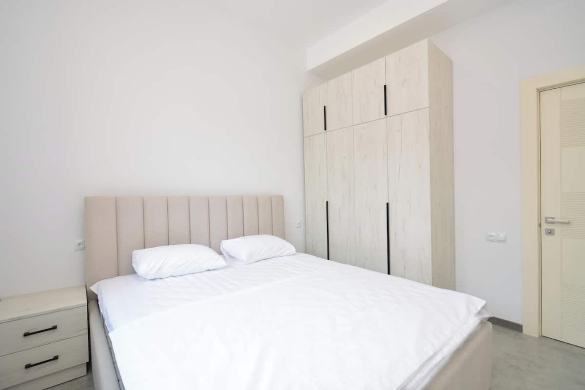 A bedroom with a bed, a nightstand, a wardrobe, and a door.