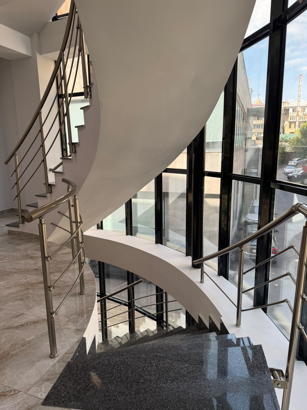 A modern spiral staircase with metal railings and glass railings, leading to an upper floor.