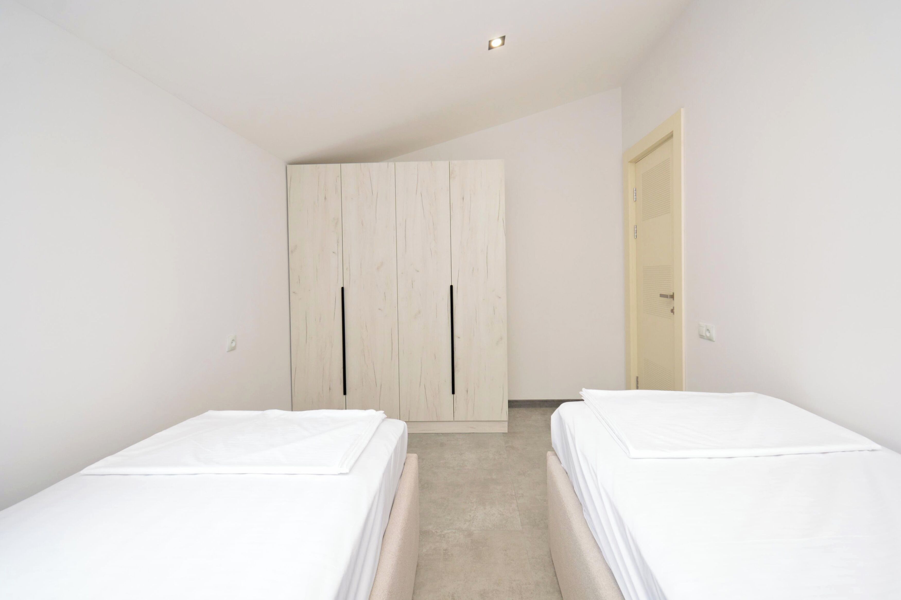 A bedroom with two beds, a wardrobe, and a door.