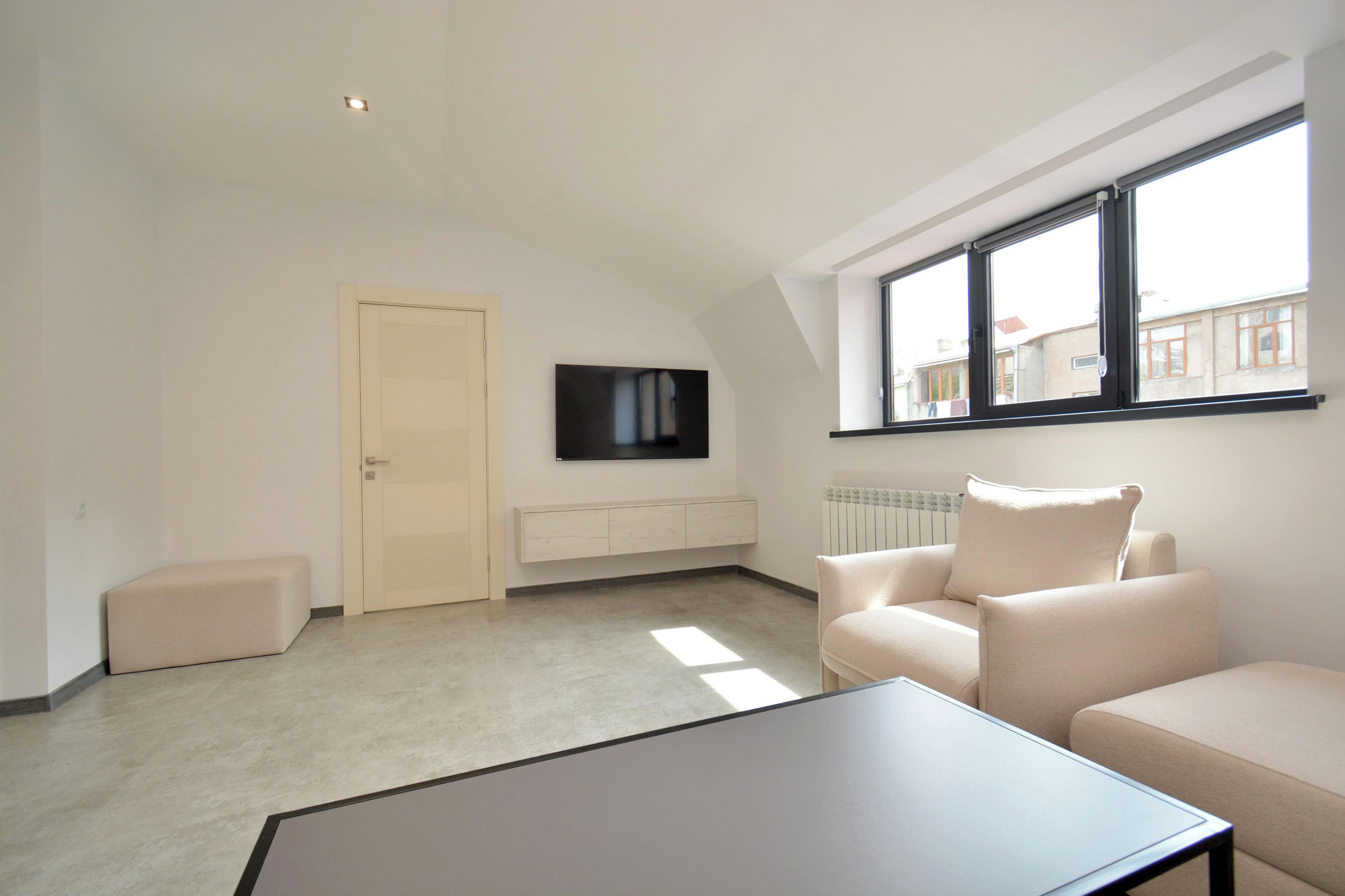 A modern living room with a sofa, a coffee table, a TV mounted on the wall, a window, and a radiator.