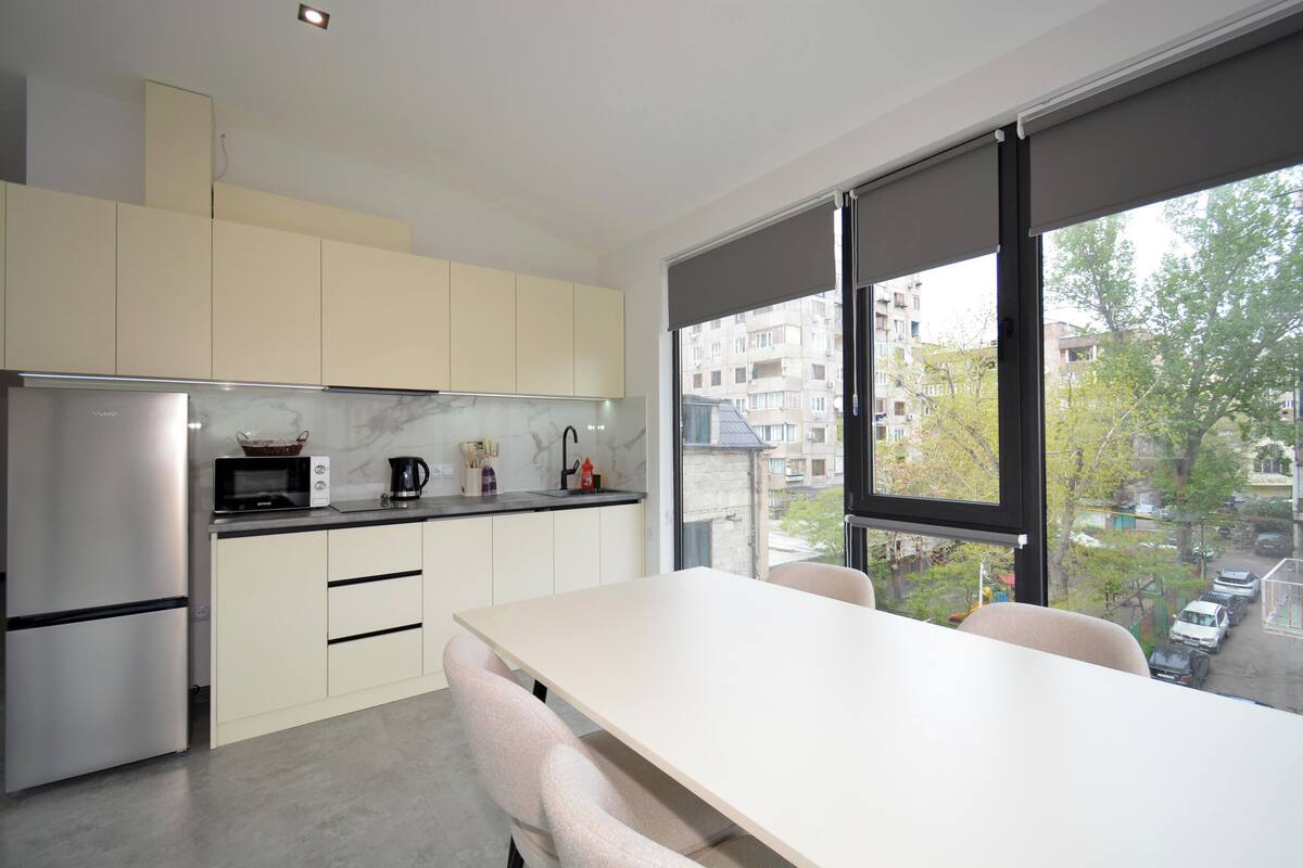 A modern kitchen with a large window, white cabinets, and a dining area with a table and chairs.