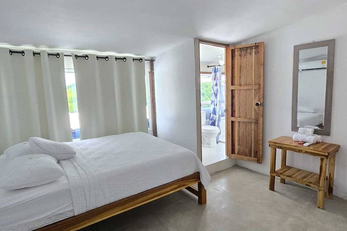 A bedroom with a bed, a wooden door, a mirror, and a small table.