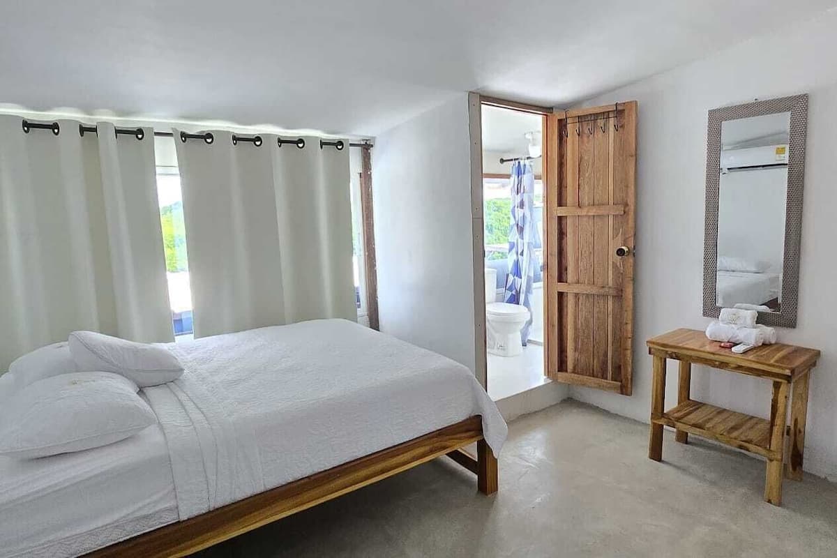 A bedroom with a bed, a wooden door, a mirror, and a small table.