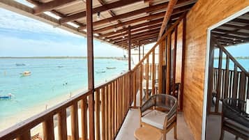 Un balcón techado con barandillas de madera, mobiliario de mimbre y vistas a la playa.