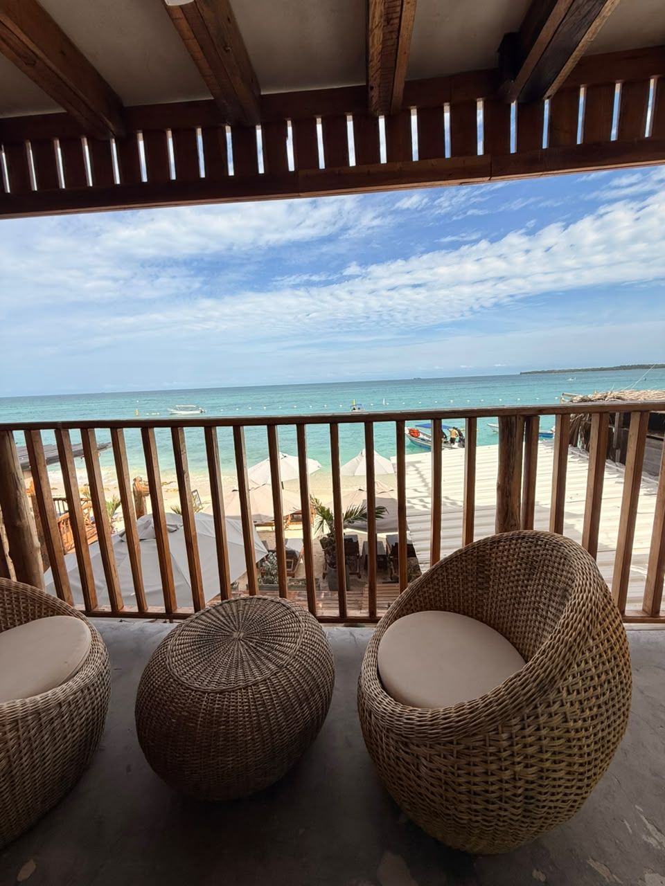 A balcony with wicker chairs and a view of the beach and ocean.