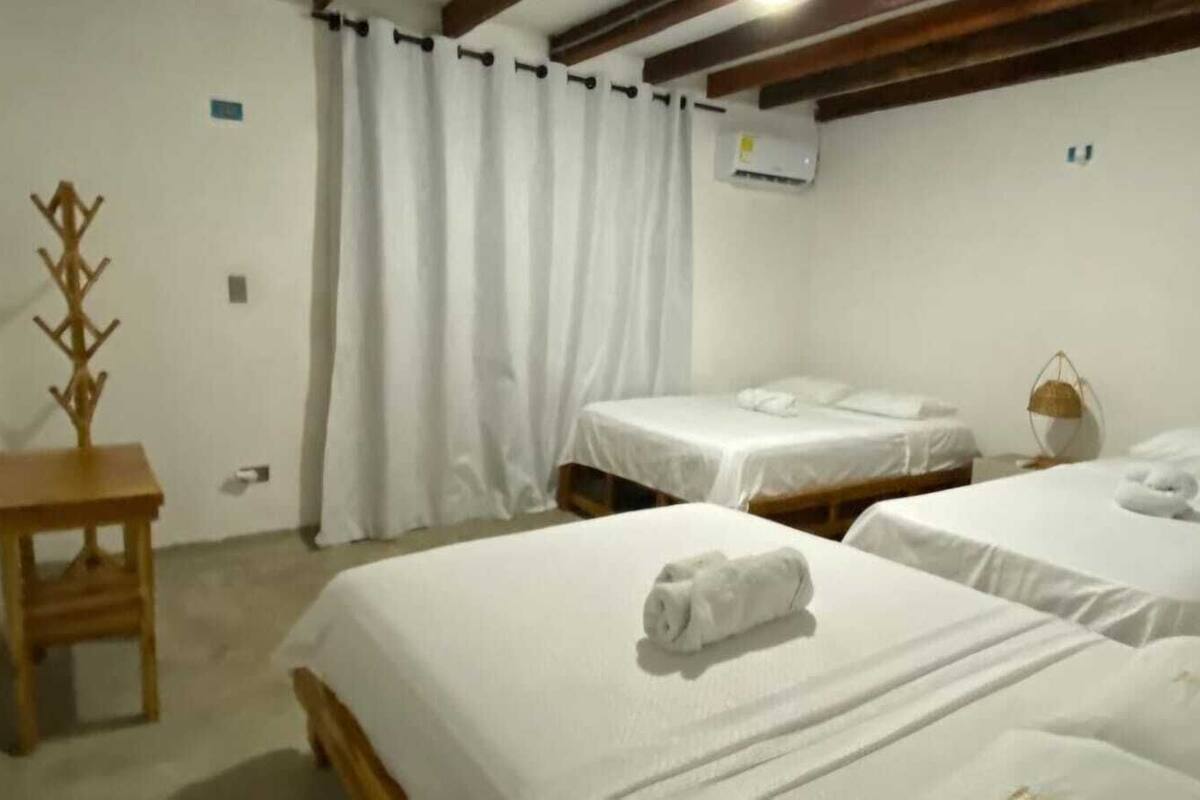 A hotel room with two beds, a wooden side table, a hanging chair, and a white curtain.