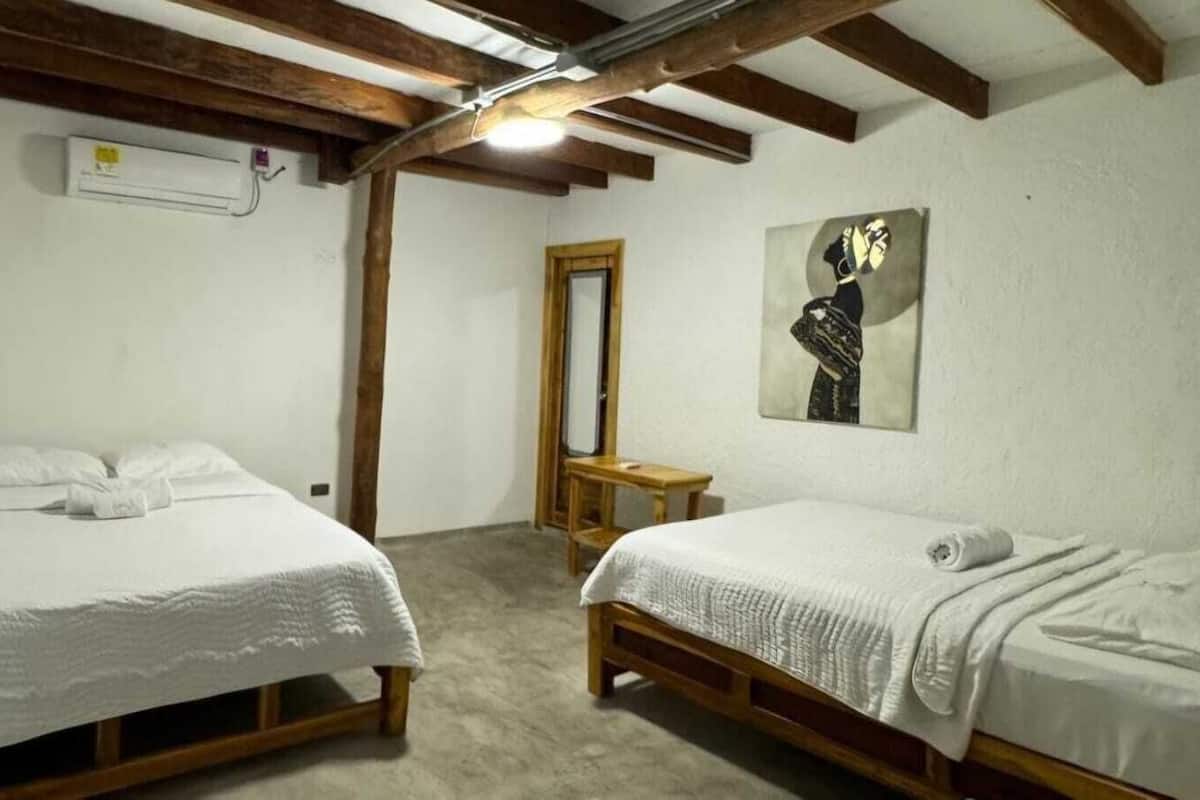 Ein Schlafzimmer mit zwei Einzelbetten, einer Holzbank, einem Spiegel und einem Gemälde an der Wand.