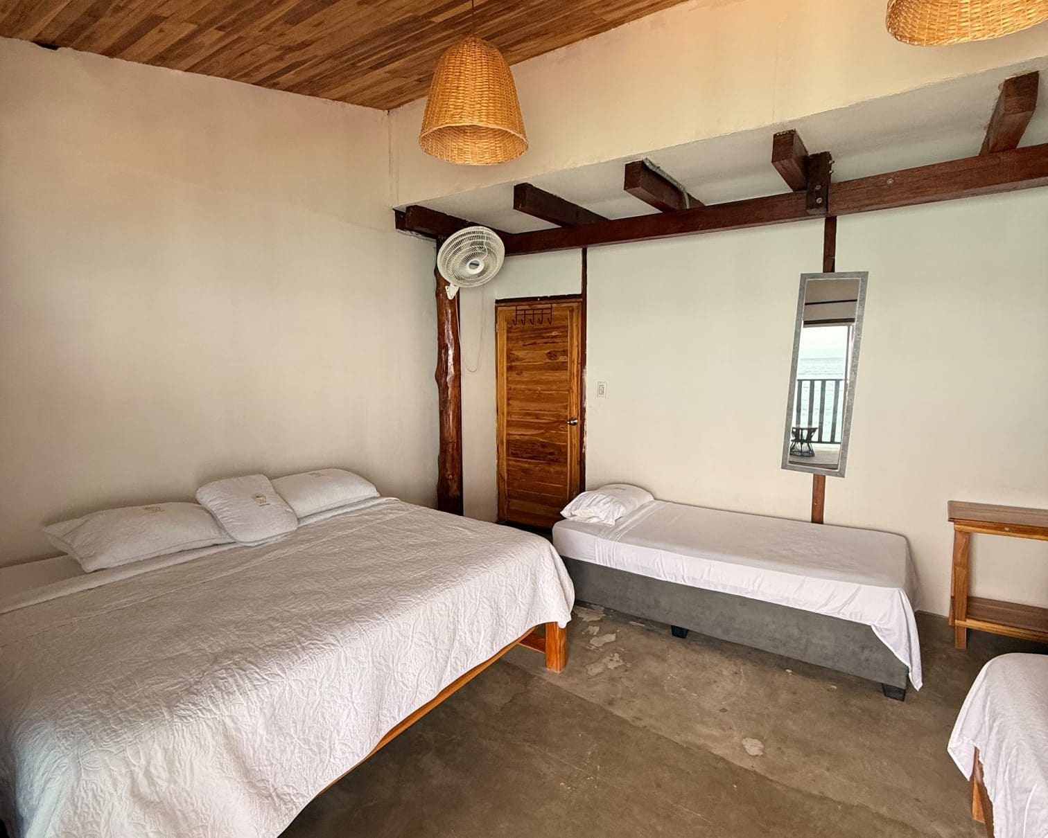 A room with two beds, a wooden ceiling, a fan, and a mirror.