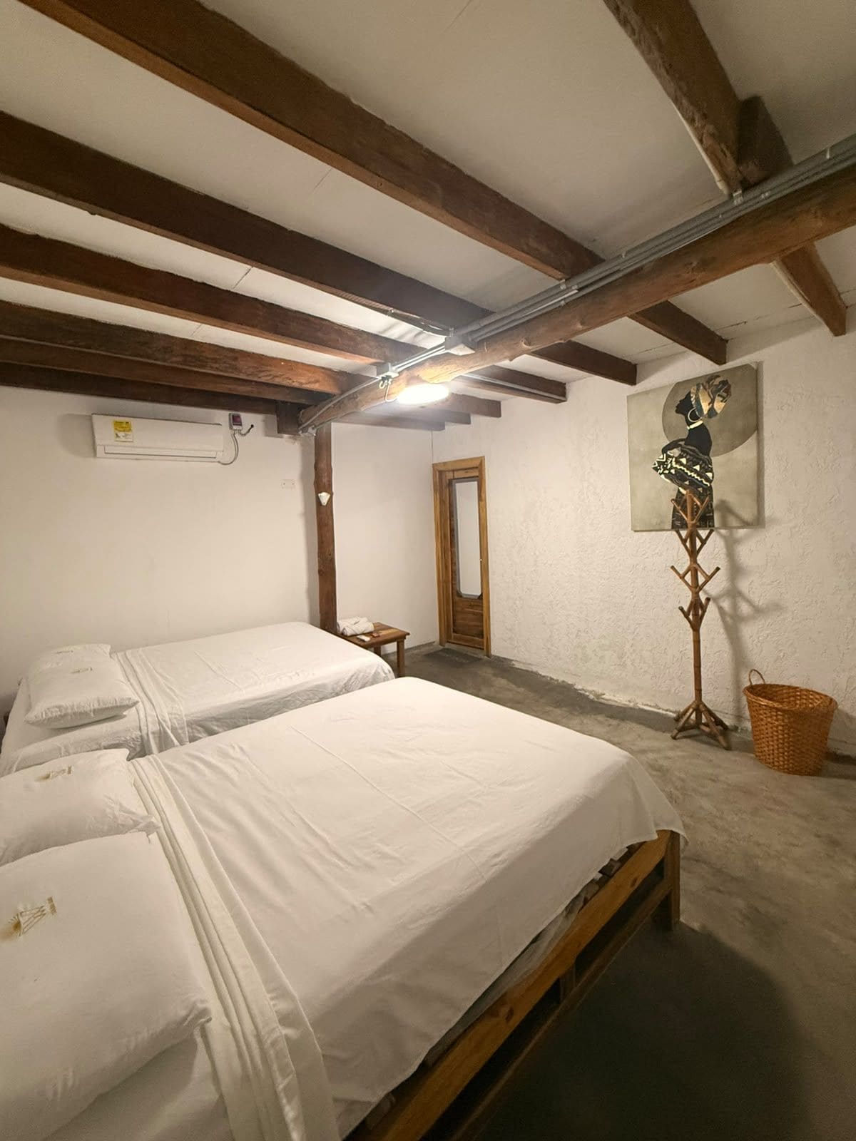 A room with two beds, a wooden floor, a ceiling fan, and a wall-mounted air conditioner.