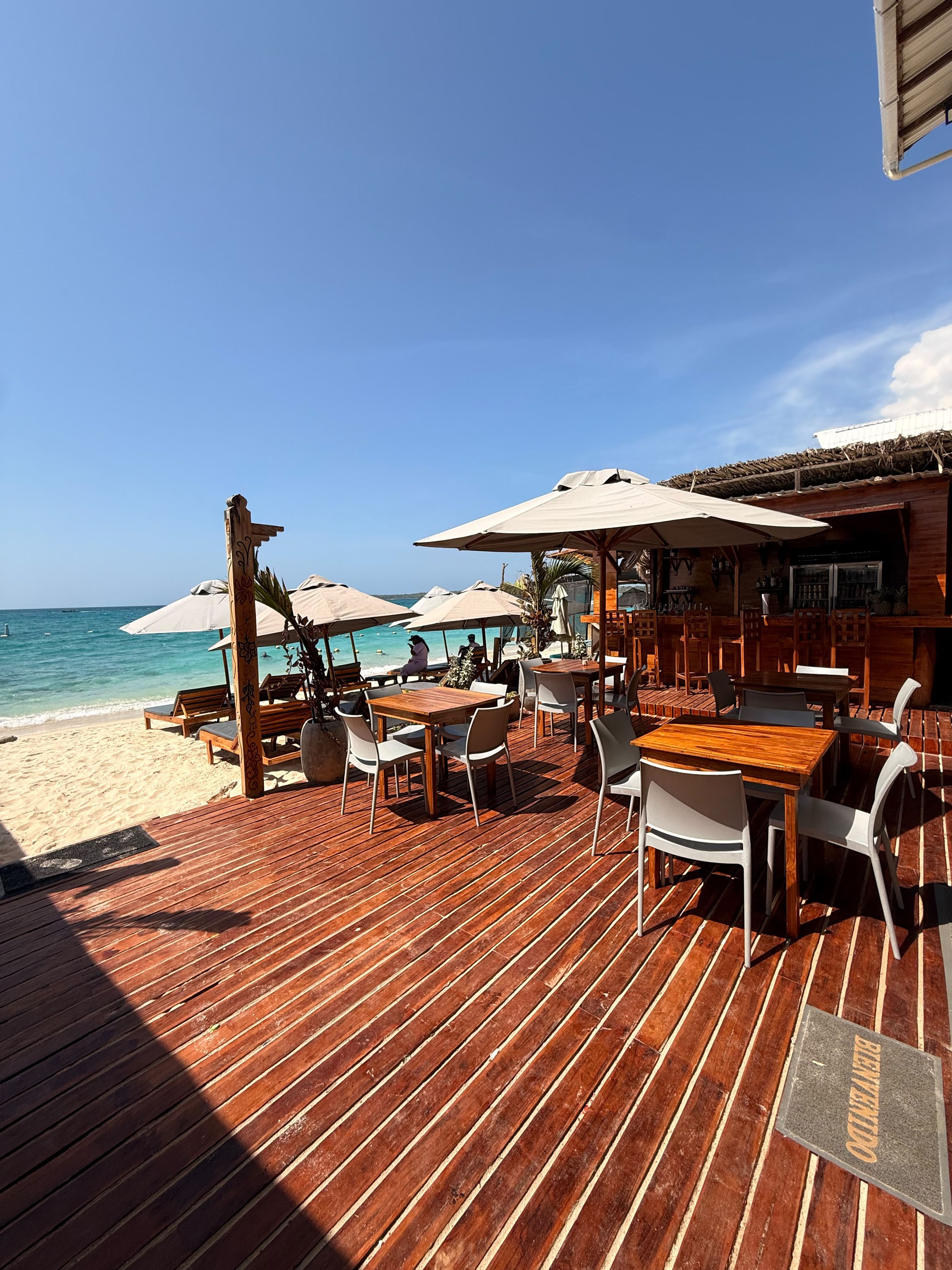 A wooden deck with tables and chairs, beach umbrellas, and a view of the ocean.