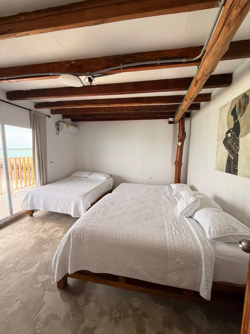 Una habitación con dos camas, vigas de madera, ventilador de techo, aire acondicionado y vistas al mar.