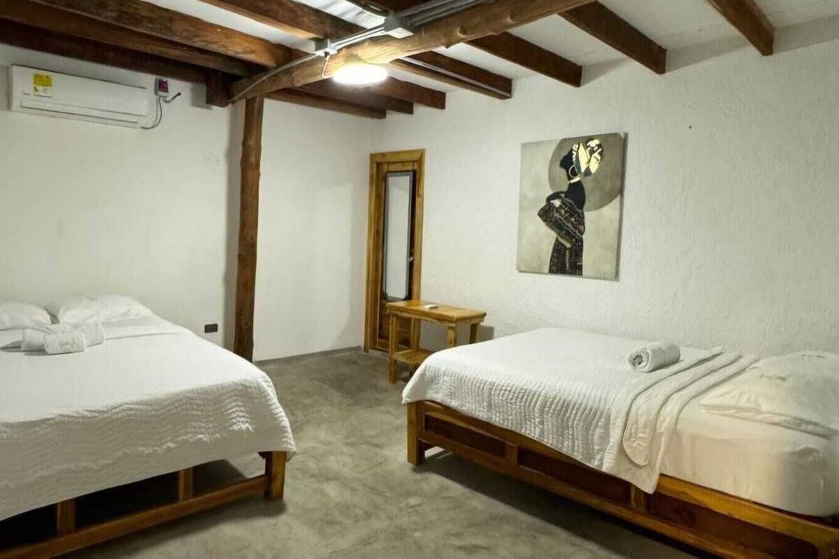 A bedroom with two single beds, a wooden bench, a mirror, and a painting on the wall.