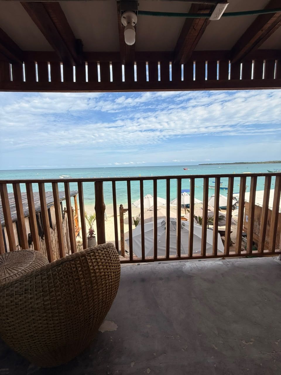 Un balcón con vista a la playa, una silla de mimbre y una barandilla.