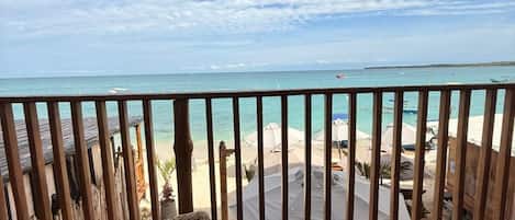 A balcony with a view of the beach, a wicker chair, and a railing.