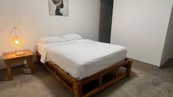 A bedroom with a wooden bed, white bedding, a nightstand with a lamp, and a wall-mounted picture.