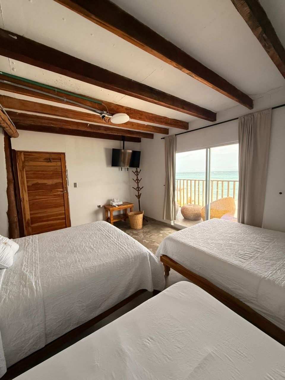 Una habitación con dos camas, vigas de madera, un televisor, una ventana con vistas y una puerta.