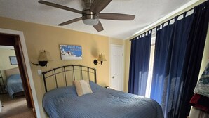 Une chambre à coucher avec un lit, un ventilateur de plafond, une porte et une fenêtre avec des rideaux.
