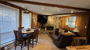 Un salon chaleureux avec une cheminée, un coin repas avec des meubles en bois et un mur d’accent en pierre.
