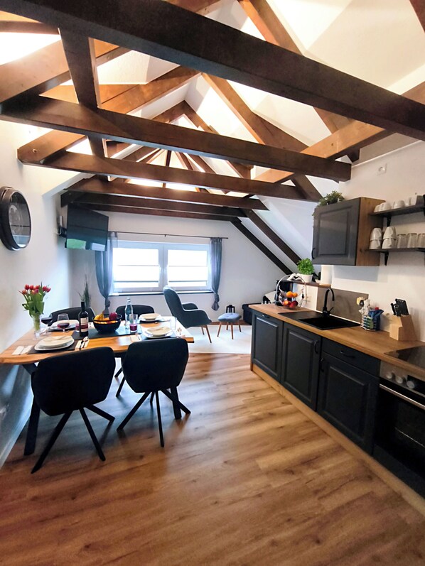 A dining area with a wooden table, chairs, and a window with curtains. - North Sea dreams Scheper - Coastal pearl (Jever)