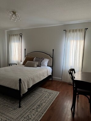 A bedroom with a bed, a table, a chair, a rug, and a ceiling light fixture.
