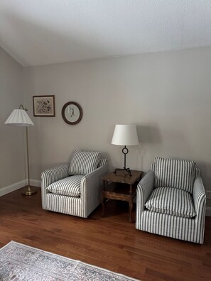 A room with two striped armchairs, a floor lamp, a side table, and a rug.