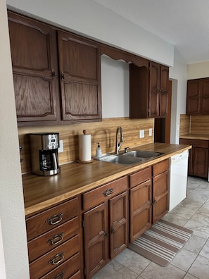 A kitchen with wooden cabinets, a coffee maker, a sink, and a dishwasher.